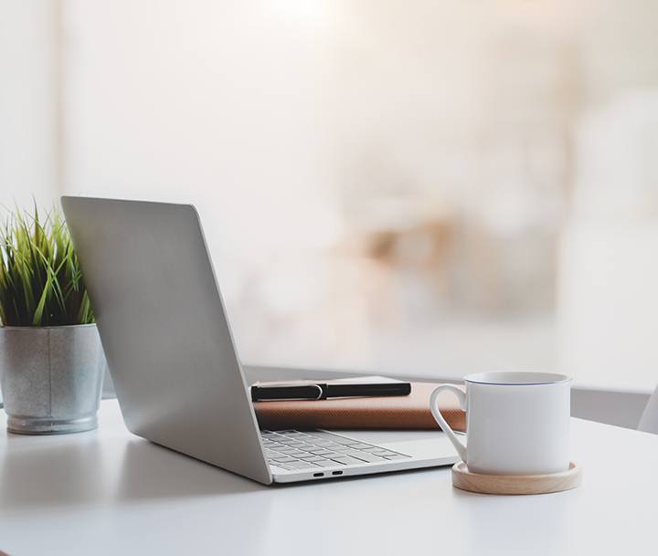 Laptop und Kaffeetasse auf einem hellen Schreibtisch